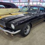 Front three-quarter view of a black and gold 1966 Shelby GT350H "Hertz Rent-A-Racer" parked at Mecum Kissimmee 2026