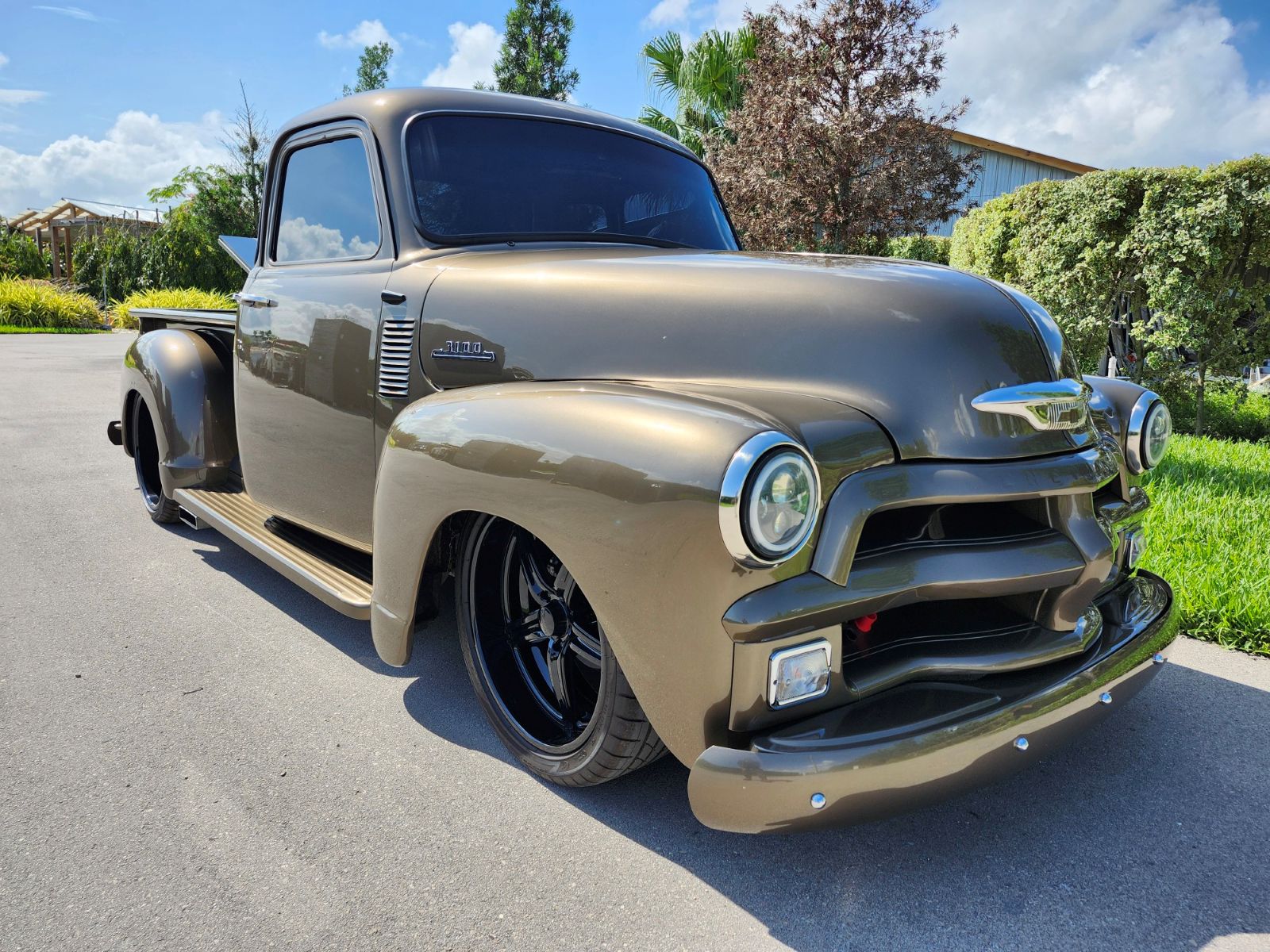 Front angle view of a restored orange 1953 Chevrolet 3100 pickup truck with chrome grille and bumpers parked at an outdoor car show.