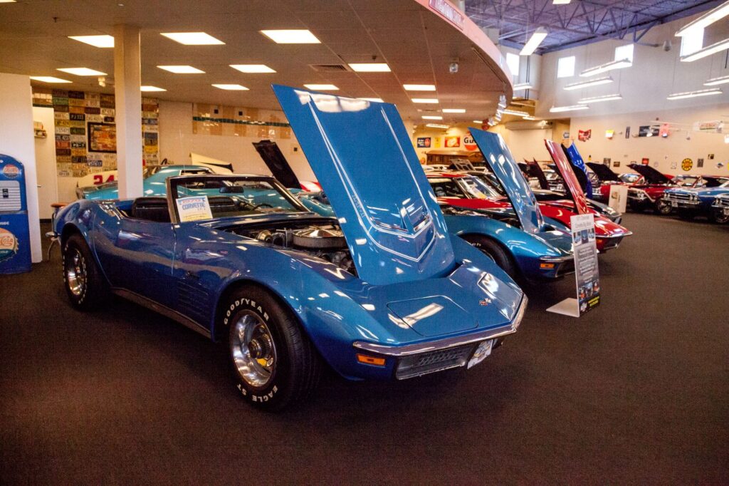 Front angle view of a bright blue 1970 Chevrolet Corvette Stingray convertible with its hood open in a showroom.