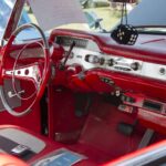 Close-up of a vibrant red 1958 Chevrolet Impala interior showing the dashboard, steering wheel, and fuzzy dice.