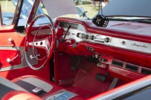 Close-up of a vibrant red 1958 Chevrolet Impala interior showing the dashboard, steering wheel, and fuzzy dice.