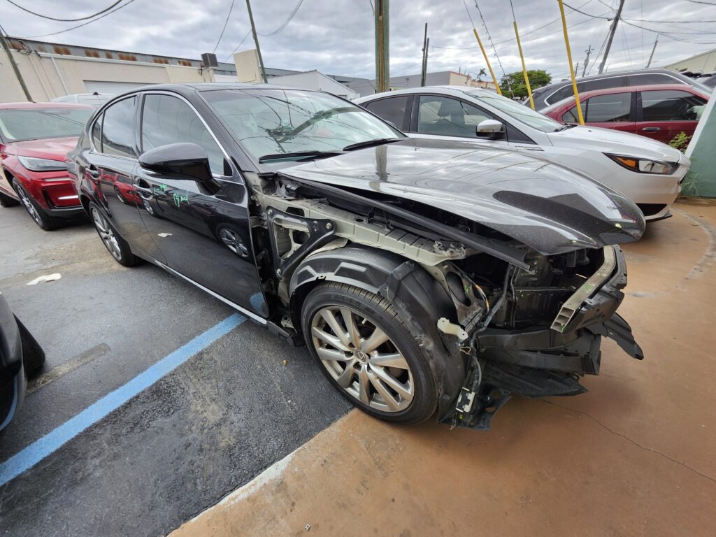 Severely damaged black 2013 Lexus gs350 with crushed front end assessed for total loss appraisal at salvage yard