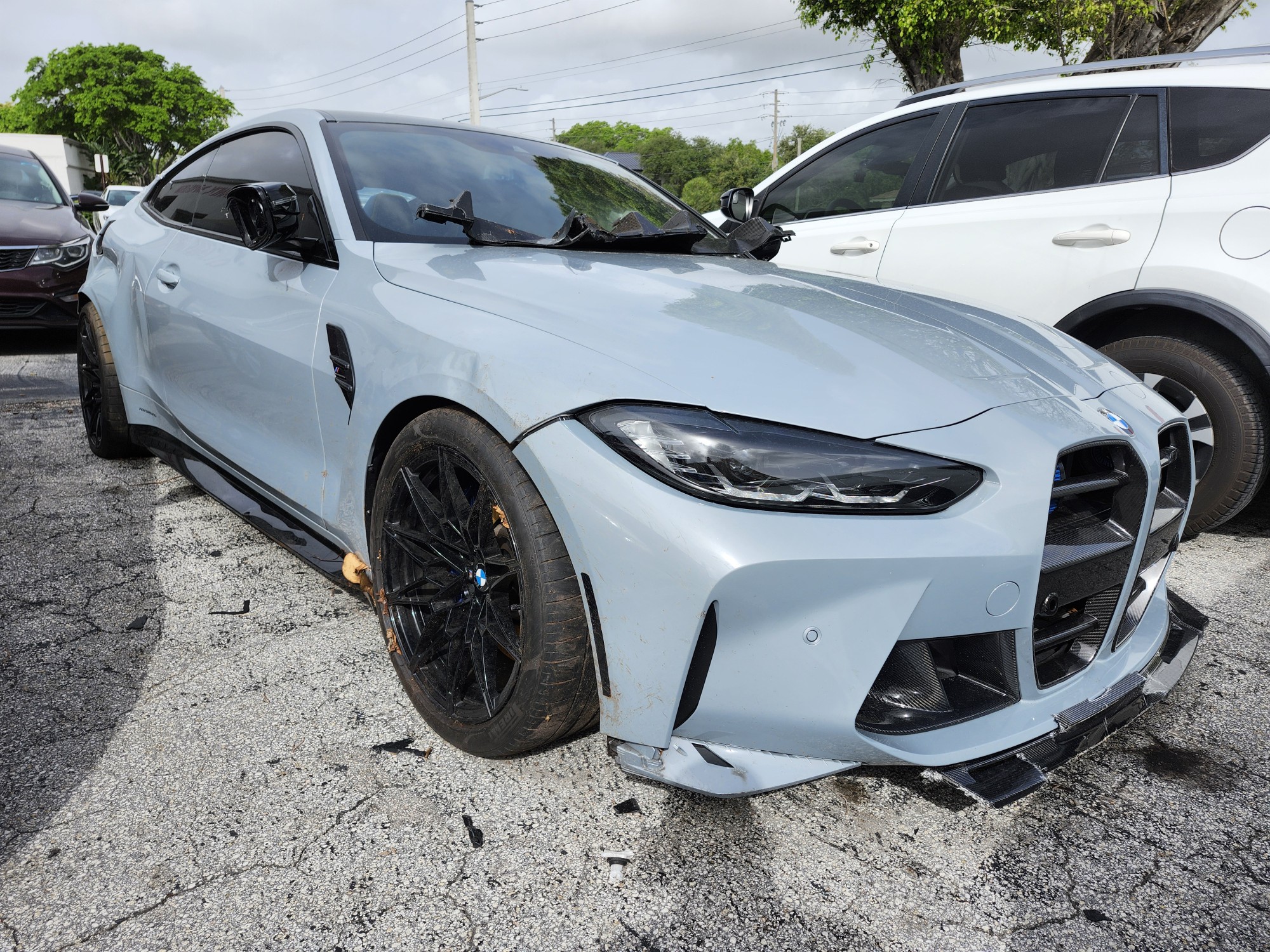 A BMW M4 Competition coupe with front-end collision damage and shattered mirror assessed for total loss appraisal in Orlando