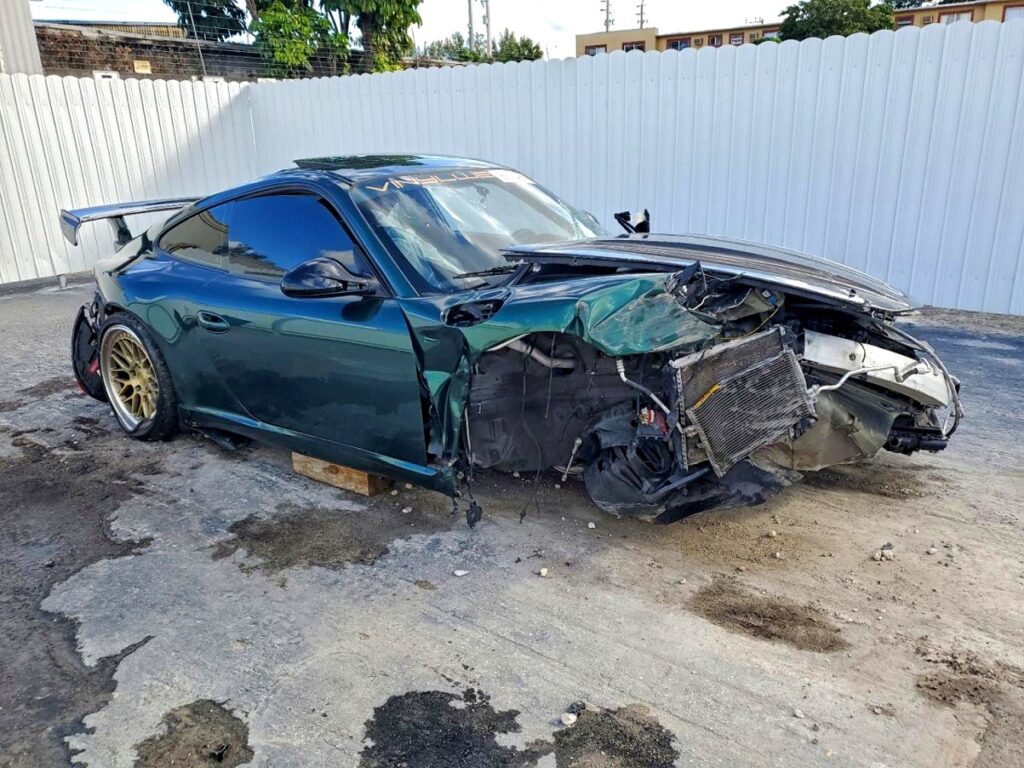 2012 Porsche 911 coupe with catastrophic front-end collision damage exposing engine components in Coral Gables for total loss appraisal