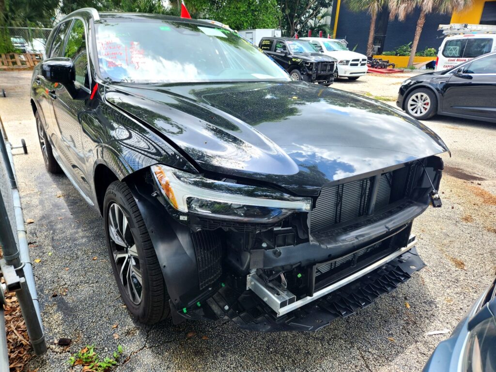 Black Volvo XC90 with detached front bumper and headlight damage, evaluated for total loss appraisal in Pompano Beach, Florida