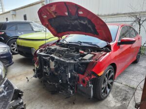 Red Honda Civic Sport with severe front-end collision damage and exposed engine bay in Royal Palm Beach for total loss appraisal