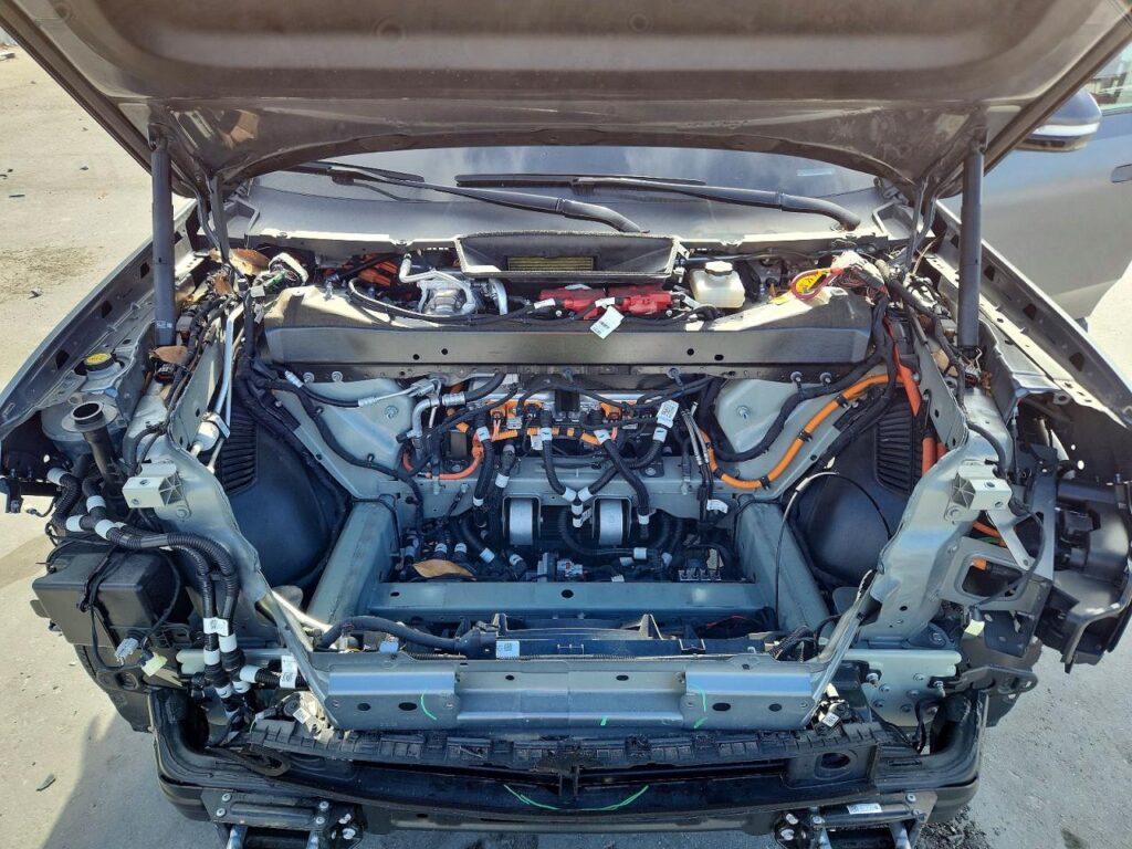 Close-up of damaged Rivian R1T front motor compartment showing exposed wiring and drivetrain components, documented for total loss appraisal in Florida